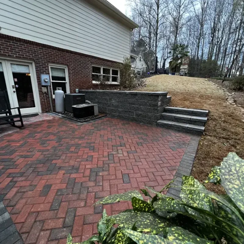 Paver herringbone pattern patio with gray retaining wall by Quiett Scapes